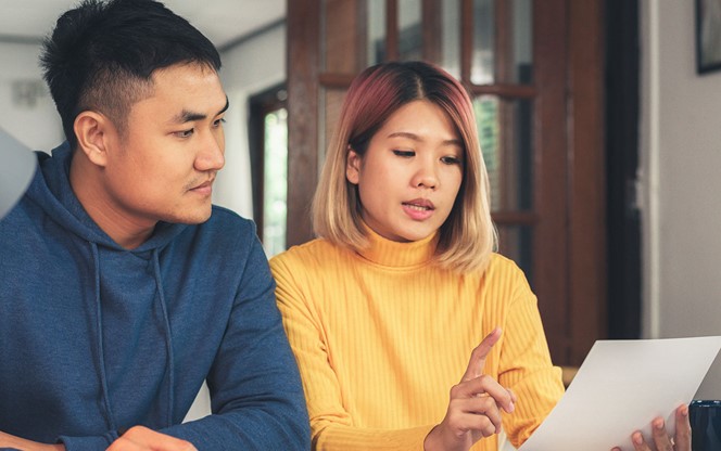 Young Asian Couple Managing Finances Reviewing Document And Accounts Using Laptop At Modern Home