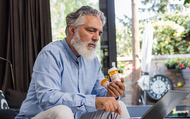 A Man In His 50S Is Holding Pill Bottles While Searching For Information Online